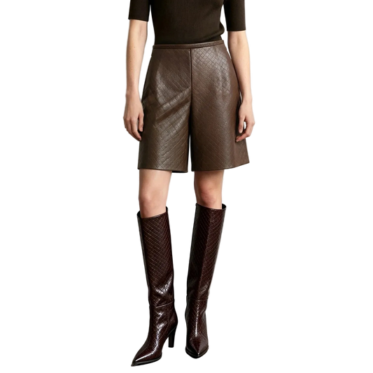 A model wearing AMII brown textured faux-leather shorts and matching dark brown knee-high boots, standing against a light gray wall.