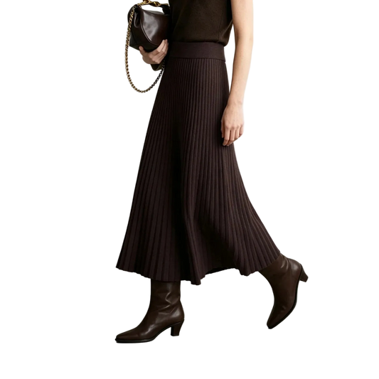A model wearing a dark brown pleated knit midi skirt, paired with matching dark brown ankle boots and holding a brown handbag, set against a minimalist studio background with the AMII brand logo in the top left corner.