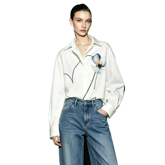 A model wearing an off-white AMII button-up shirt with a black line-art floral design and a blue flower applique, paired with high-waisted blue jeans against a dark studio background.