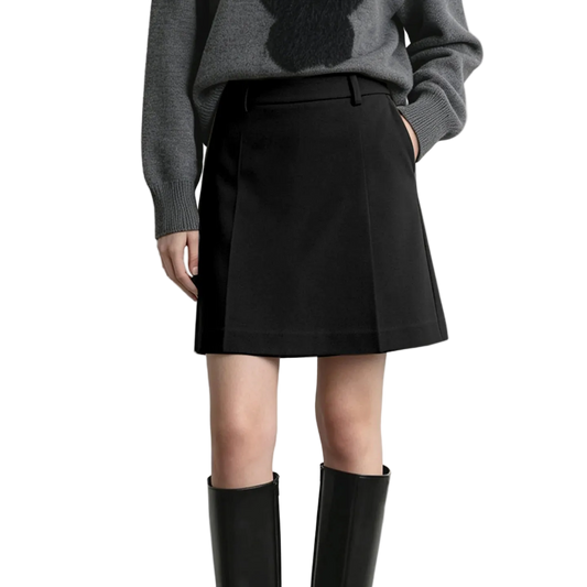 A model wearing a black A-line mini skirt with side pockets, paired with a gray knit sweater and black knee-high boots, shown from the chest down against a light gray studio background.