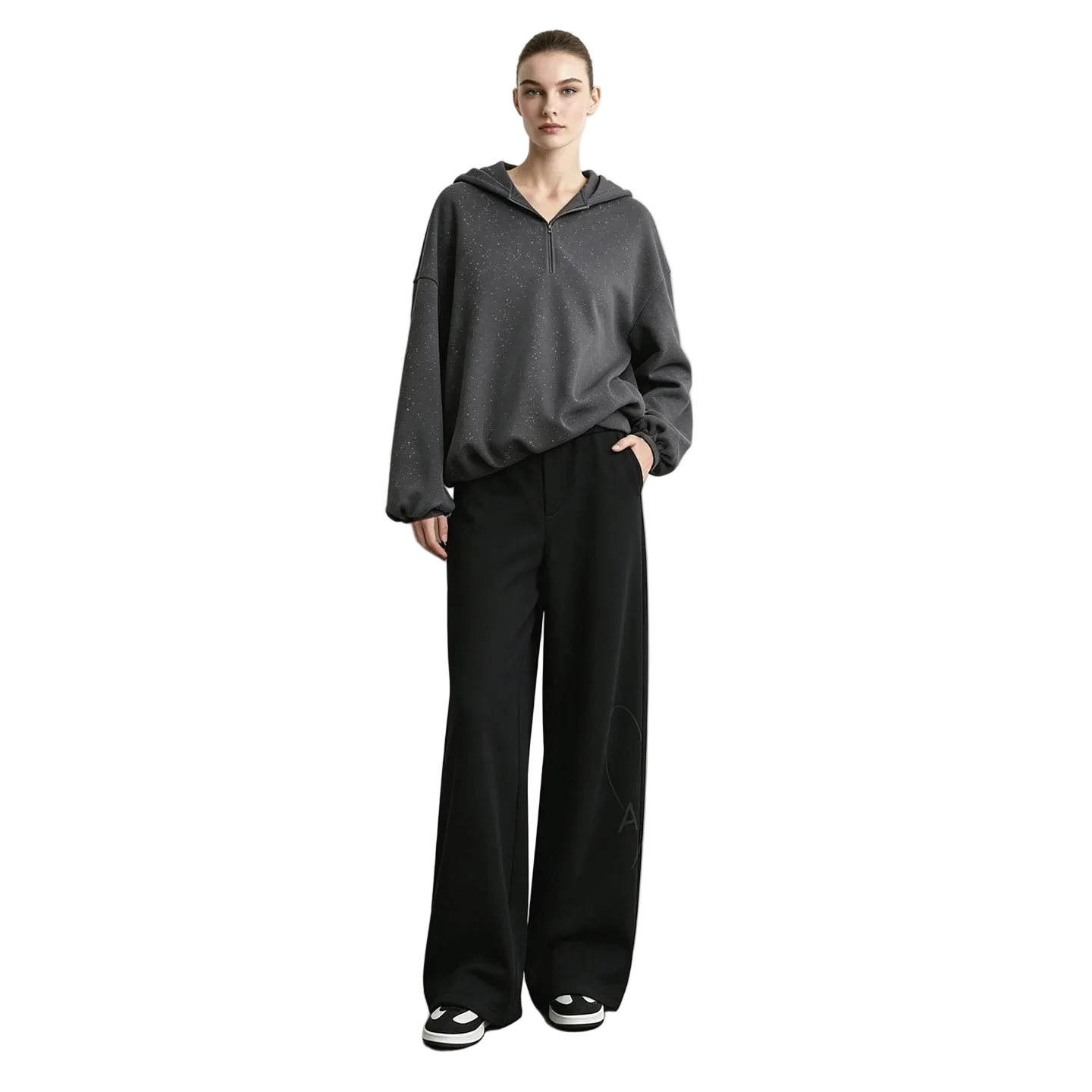 A model stands against a light gray wall wearing a dark gray half-zip hoodie, black wide-leg pants, and black-and-white sneakers.