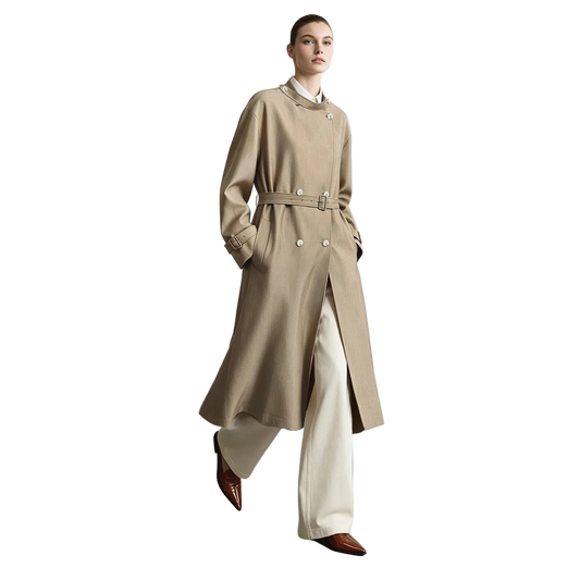 A model wearing a long beige trench coat with a matching belt, paired with cream wide-leg trousers and brown pointed shoes, standing in a minimalist studio setting with the AMII brand logo in the top left corner.