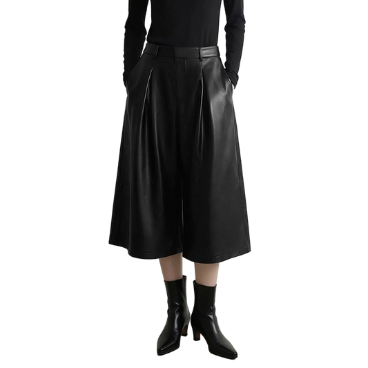 A model wearing a black faux leather wide-leg cropped skirt with pleats, paired with a black long-sleeve top and black pointed-toe ankle boots. The AMII brand logo is visible in the top left corner against a light gray studio background.