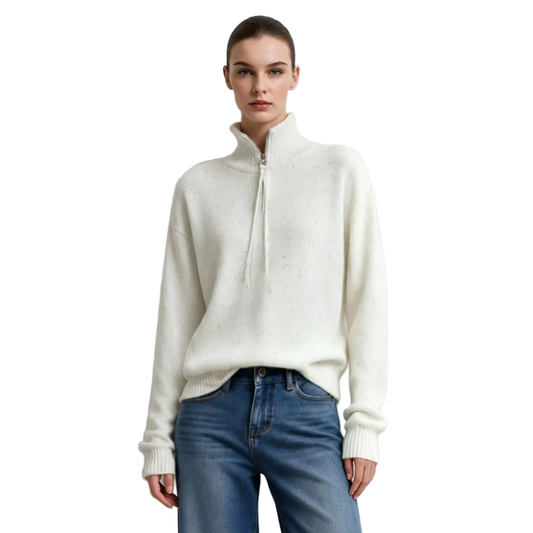 A model wearing an AMII cream-colored half-zip mock neck sweater and blue jeans, standing against a plain light gray wall.