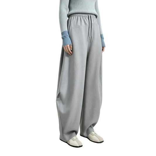 A model wearing light gray wide-leg sweatpants with a drawstring waist, paired with a light blue ribbed sweater and white slip-on shoes. The AMII brand logo is visible in the top left corner against a light gray studio background.